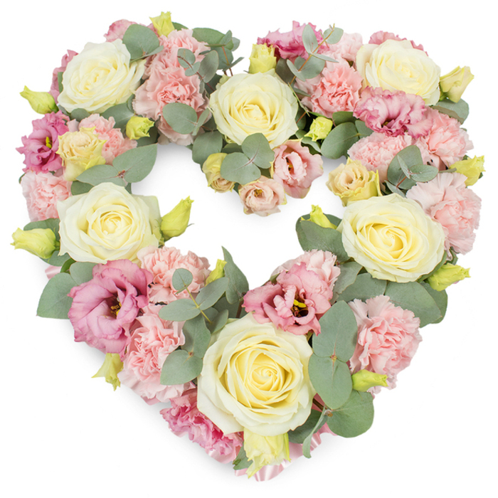 A luxurious heart-shaped floral wreath is presented against a crisp white background, its contours perfectly defined by an intricate blend of pastel blooms and soft greenery, reminiscent of the thoughtful sympathy flowers often chosen by families in Northolt. The heart is packed so densely that every inch is covered in petals, giving a cushioned, almost quilted effect that feels both protective and embracing. Large cream and pale yellow roses are positioned as focal points around the form, their tightly layered petals unfurling gracefully and catching the light with a gentle satin sheen. Between these generous blooms, light pink carnations cluster in generous groups, their frilled edges creating a delicate, rippling texture that softens the entire piece. Interspersed through the pastel canvas are deeper rose-pink and mauve lisianthus flowers, their looser, more open petals adding a gentle sense of movement, as if the blooms have settled naturally into place. Silvery-green eucalyptus leaves thread their way around and beneath the flowers, the rounded foliage peeking out just enough to frame the heart and introduce subtle contrast. Small yellow-green buds are dotted throughout, suggesting the freshness of flowers arranged that same morning for a service at Northolt's local cemetery or crematorium. The overall palette of creams, blush pinks, and muted greens conveys quiet tenderness and heartfelt affection, ideal for honouring a loved one's memory. This heart-shaped wreath feels especially suited for funeral tributes, celebration of life ceremonies, or anniversaries of passing, offering a gentle, elegant expression of sympathy to families across Northolt and the surrounding neighbourhoods.